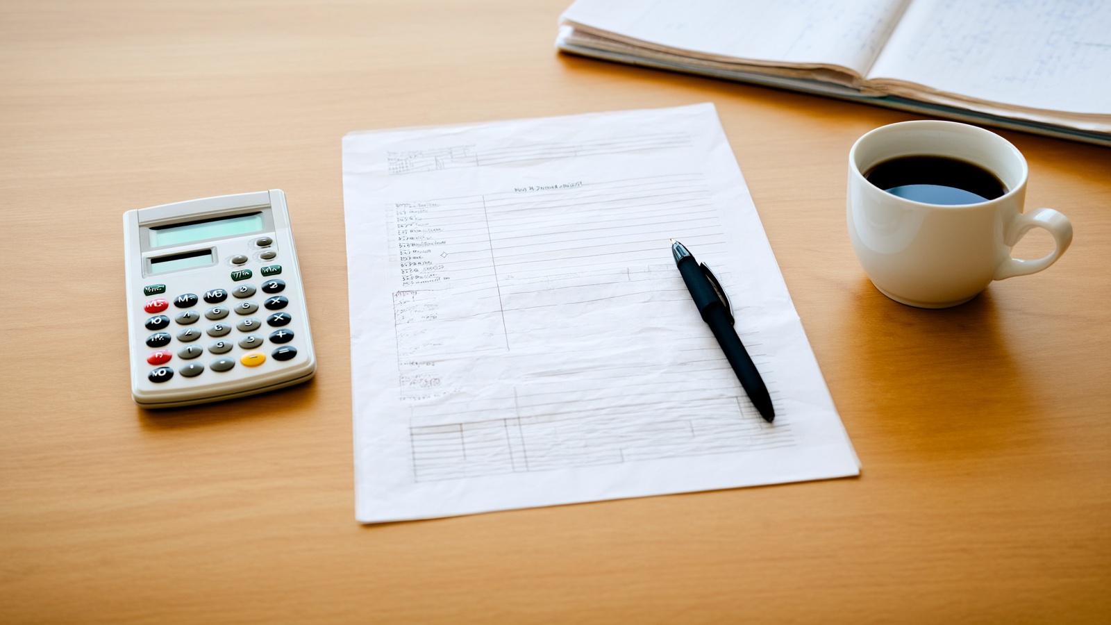 Clean desk with an invoice, pen, calculator and coffee in bright natural light