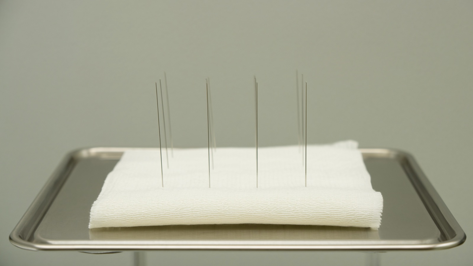Fine filiform needles on a stainless steel tray in a clinic setting